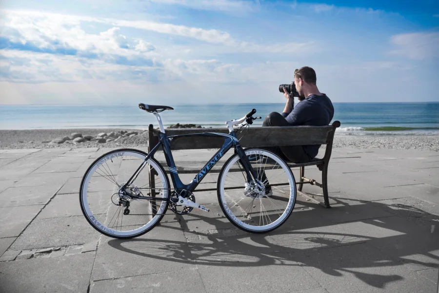 Fotograf på en bænk med cykel ved stranden