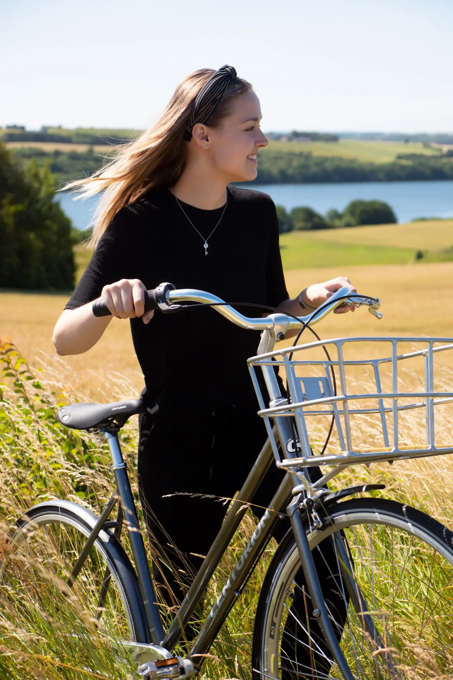 Kvinde med cykel i kornmark ved sø